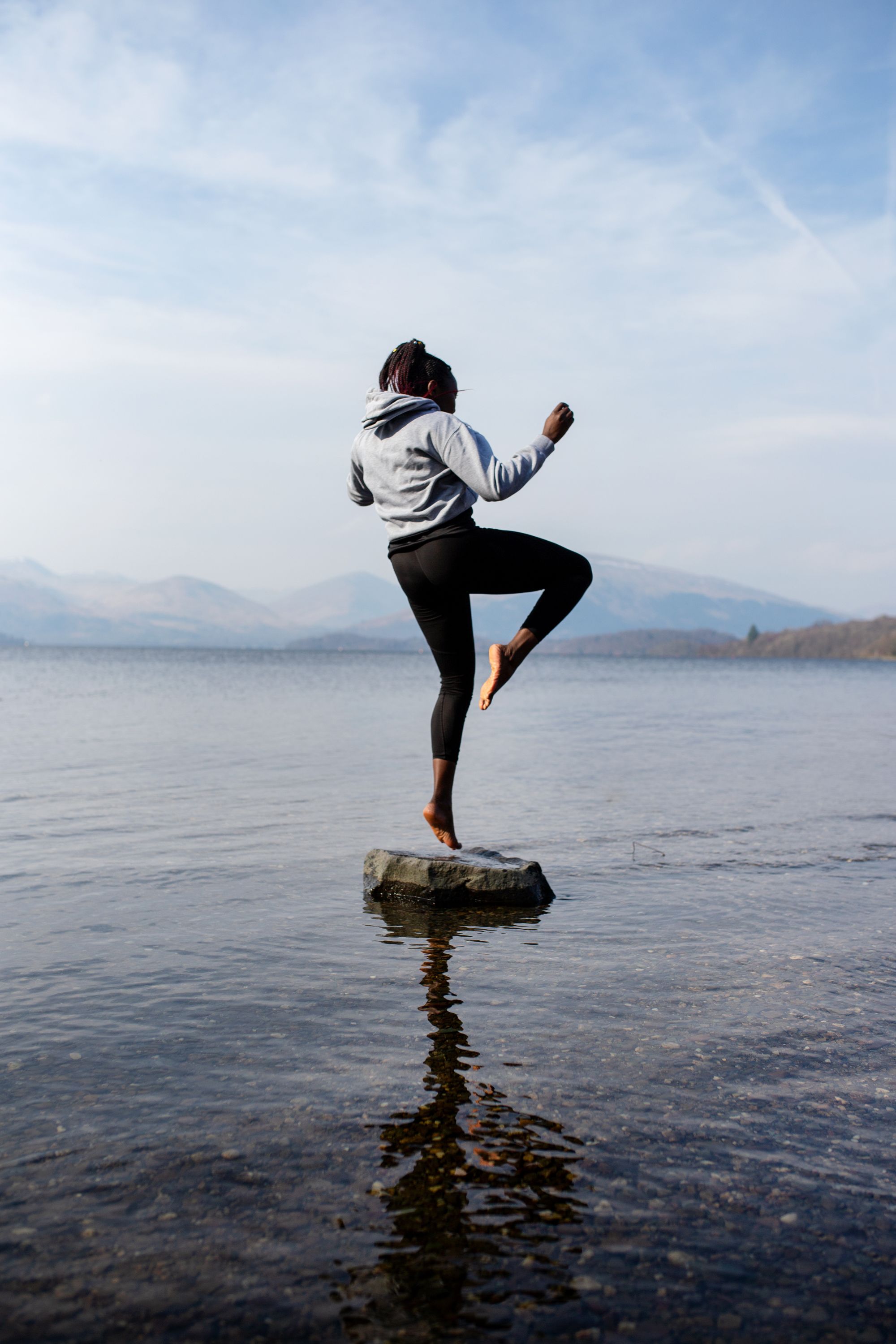 A woman standing on a rock in a loch facing the mountains